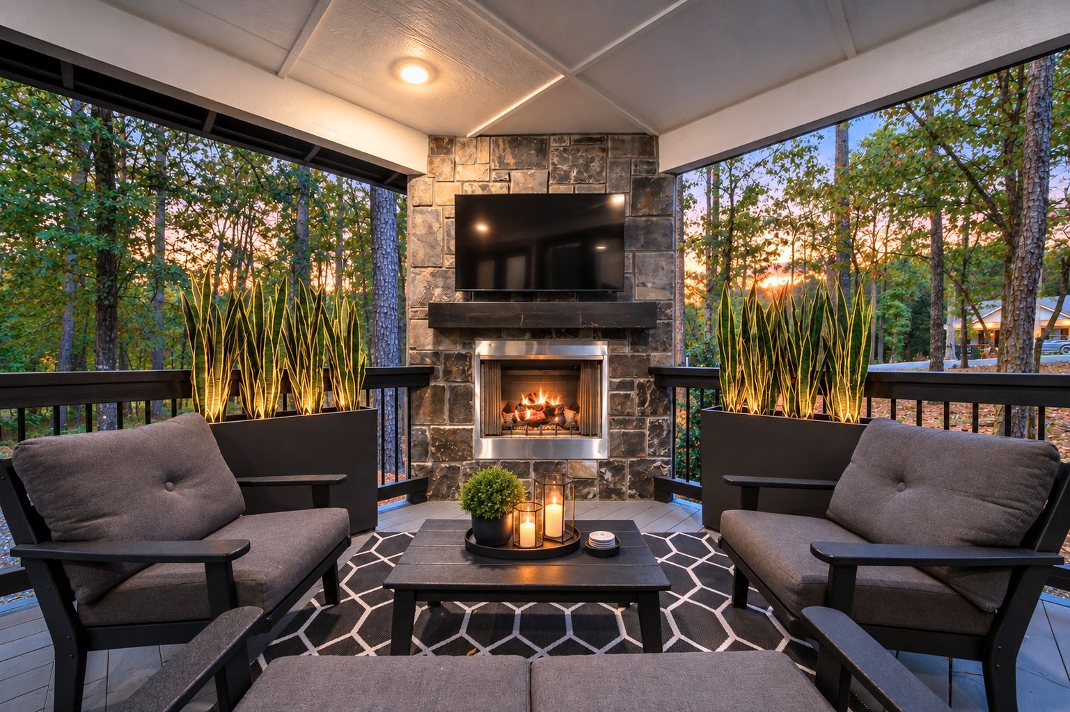 An outdoor seating area with a stone fireplace, two cushioned chairs, and a table with a candle centerpiece.