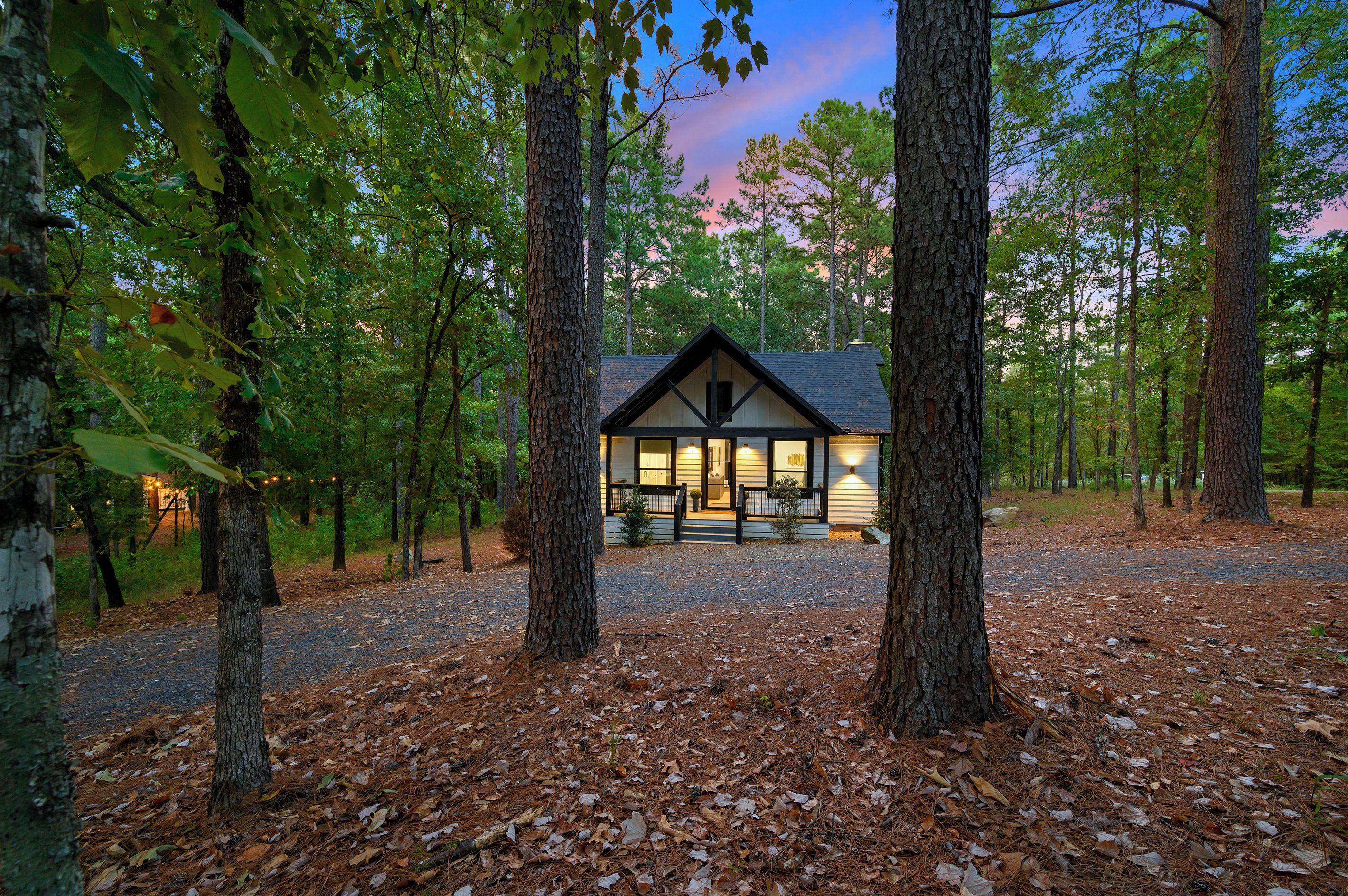 A cabin with a porch, surrounded by trees and a gravel path.