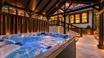 Un jacuzzi con iluminación integrada, una terraza de madera y una escalera que lleva a una casa con ventanas grandes.