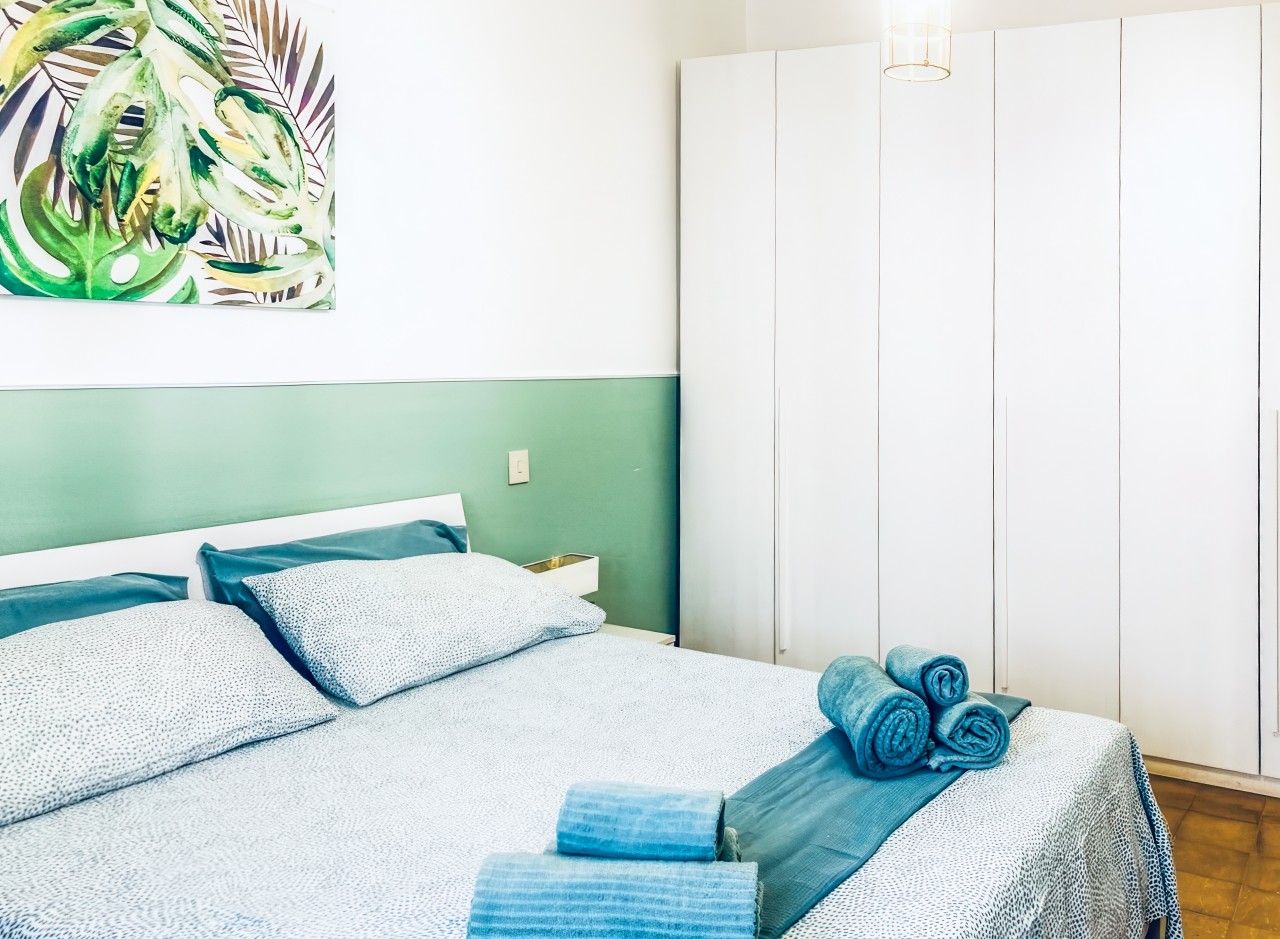 Een slaapkamer met een bed, kussens, een nachtkastje, een lamp en een kledingkast.