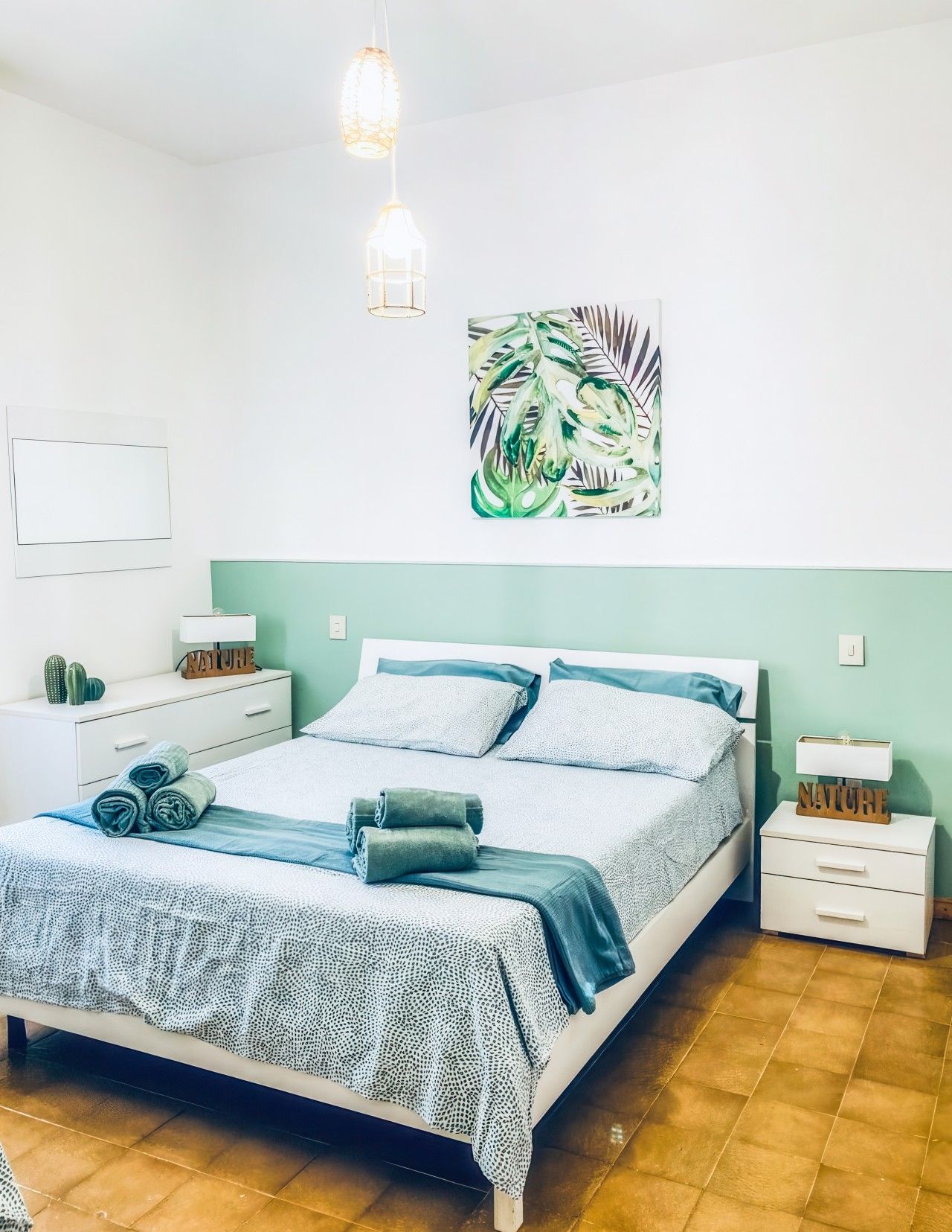 Een slaapkamer met een bed, twee nachtkastjes, een wandlamp en een ingelijste botanische print.