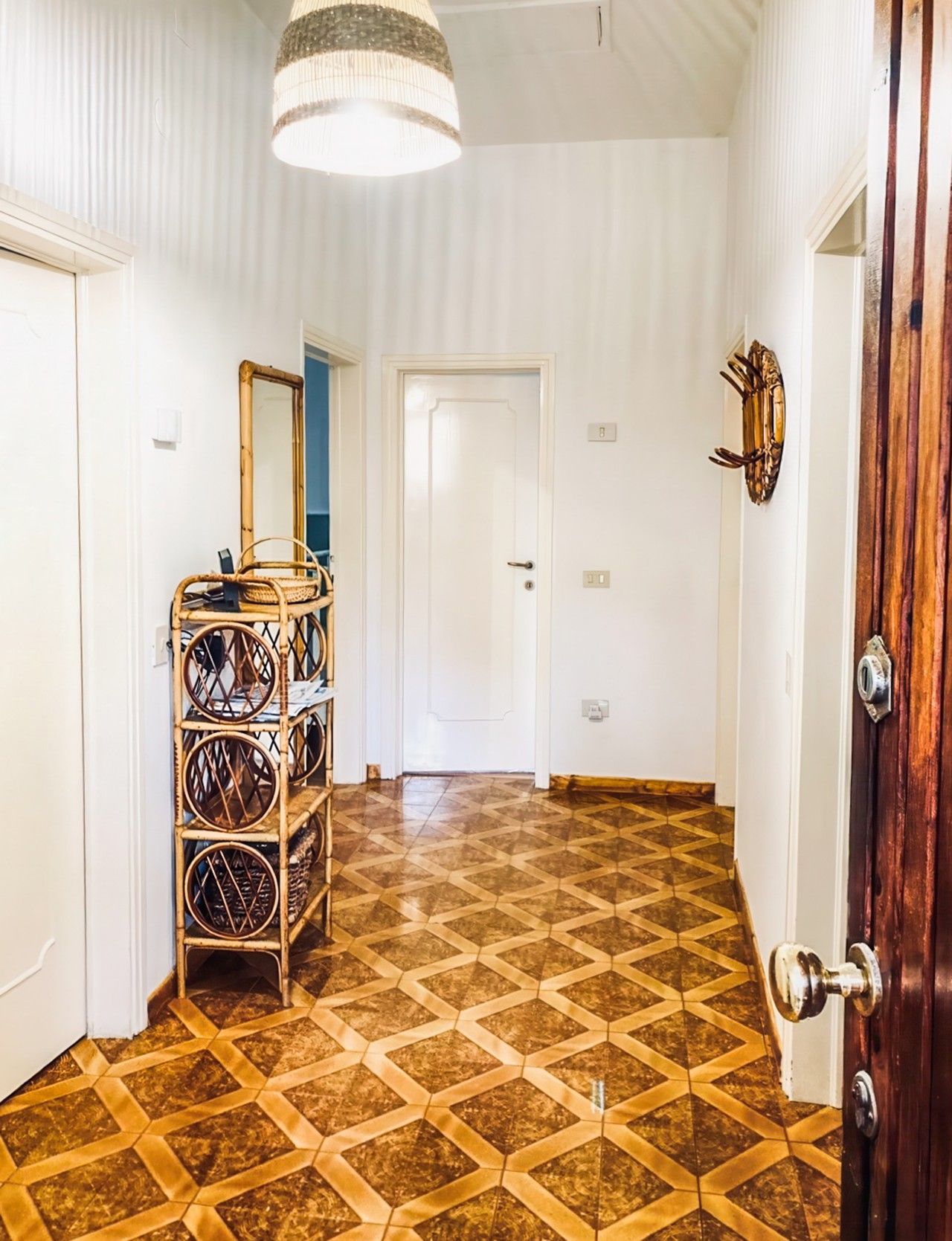 Un couloir avec un sol à motifs, un miroir, un panier en osier et une porte dotée d’une poignée rustique.
