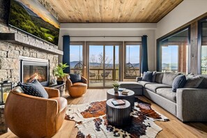A modern living room with a fireplace, leather sofas, a round coffee table, and a large window overlooking a deck. - Serenity Summit | Indoor Pool, Hot Tub, GameRoom! (Sevierville)