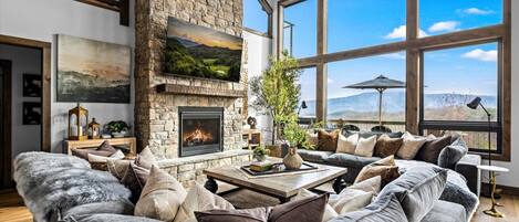 Amplia sala de estar con chimenea de piedra, ventanas grandes y vistas al exterior.