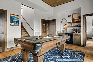 A pool table in a room with a wooden ceiling, a staircase, and a kitchen area. - Serenity Summit | Indoor Pool, Hot Tub, GameRoom! (Sevierville)