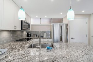 A glass cooktop and a coffee station line up under the gray subway tile, ready before anyone's fully awake. - Haleakala Shores A206 by Gather - Remodeled Condo Across from Kamaole Beach III (Kihei)