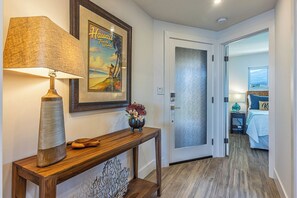 Um corredor com um console de madeira, uma luminária, um quadro emoldurado e uma porta que dá para um quarto.