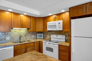 A kitchen with wooden cabinets, a microwave, stove, and a refrigerator. - Maui Banyan H306 by Gather - Ocean-View Lanai w/ AC, Walk to Beach (Kihei)