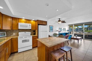A kitchen with wooden cabinets, a white stove, and a marble countertop. - Maui Banyan H306 by Gather - Ocean-View Lanai w/ AC, Walk to Beach (Kihei)