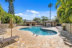 A swimming pool with lounge chairs and umbrellas, surrounded by palm trees and a stone patio. - Maui Banyan H306 by Gather - Ocean-View Lanai w/ AC, Walk to Beach (Kihei)