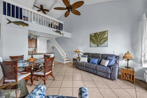A spacious living area with a dining table, chairs, a sofa, and a staircase leading to an upper level. - Maui Vista 2420 by Gather - Kihei Loft Condo w/ Pool, Walk to Kamaole Beaches (Kihei)