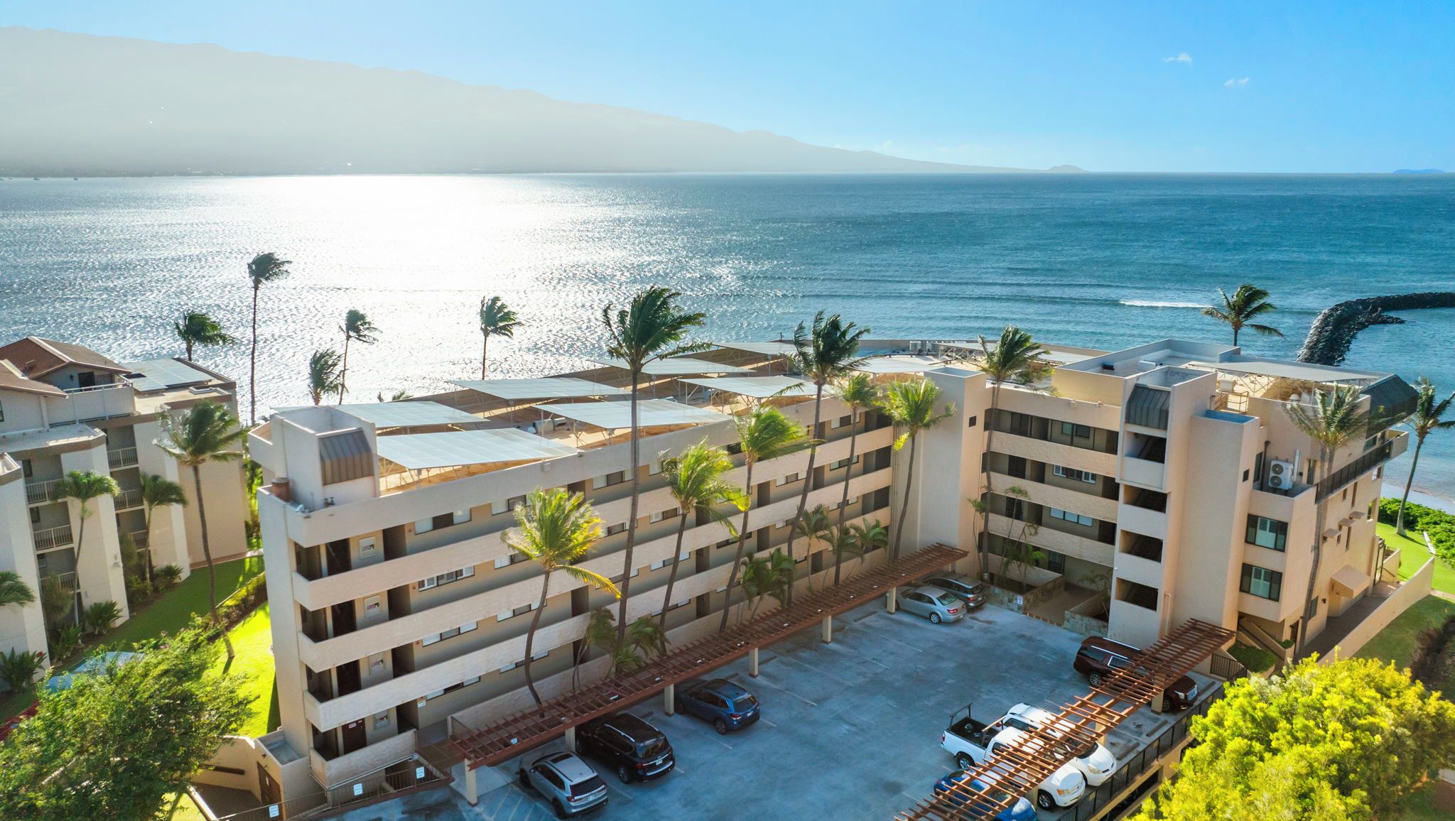From above, Milowai's rooftop solar panels and parking pergolas fill the space between the road and the rocky shoreline below.