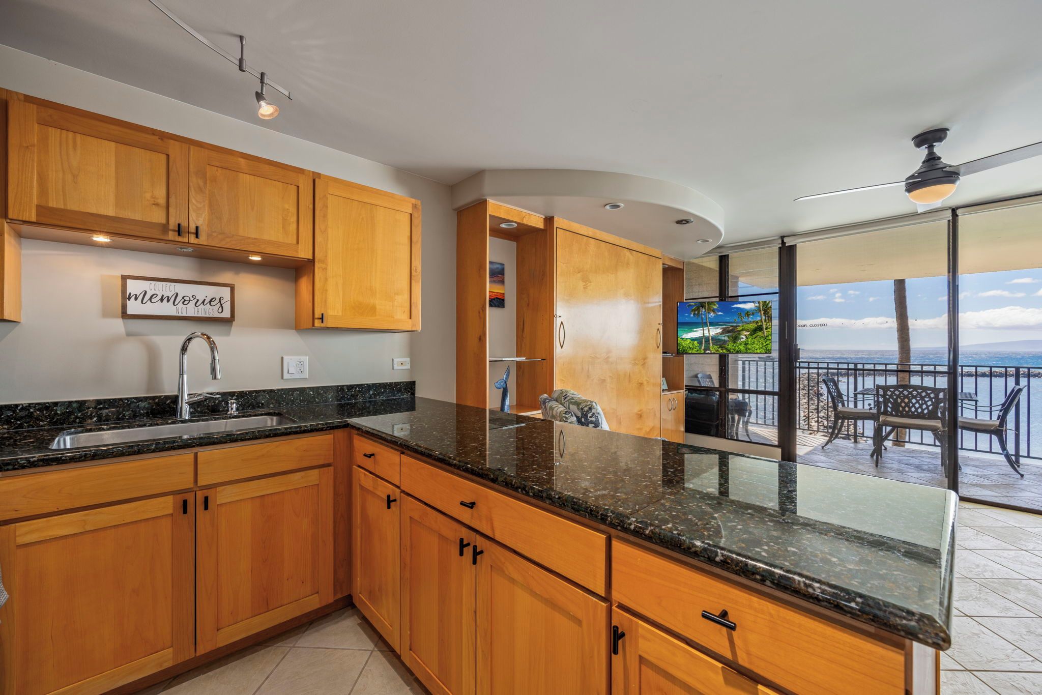 A modern kitchen with wooden cabinets, a granite countertop, and a built-in TV.