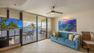 A room with a sliding glass door leading to a balcony, a blue sofa, a ceiling fan, and a large abstract painting.