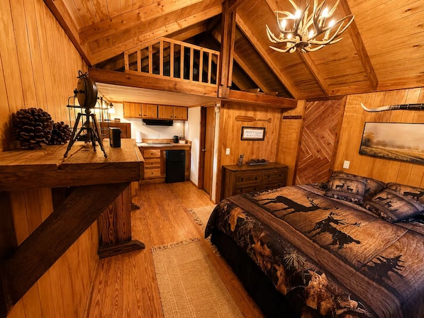 Interior rústico de una cabaña con un dormitorio en loft, kitchenette y comedor.