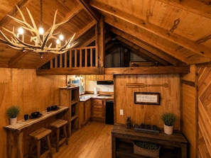 Un interior rústico de madera con comedor, cocina y una araña hecha con cuernos de ciervo.