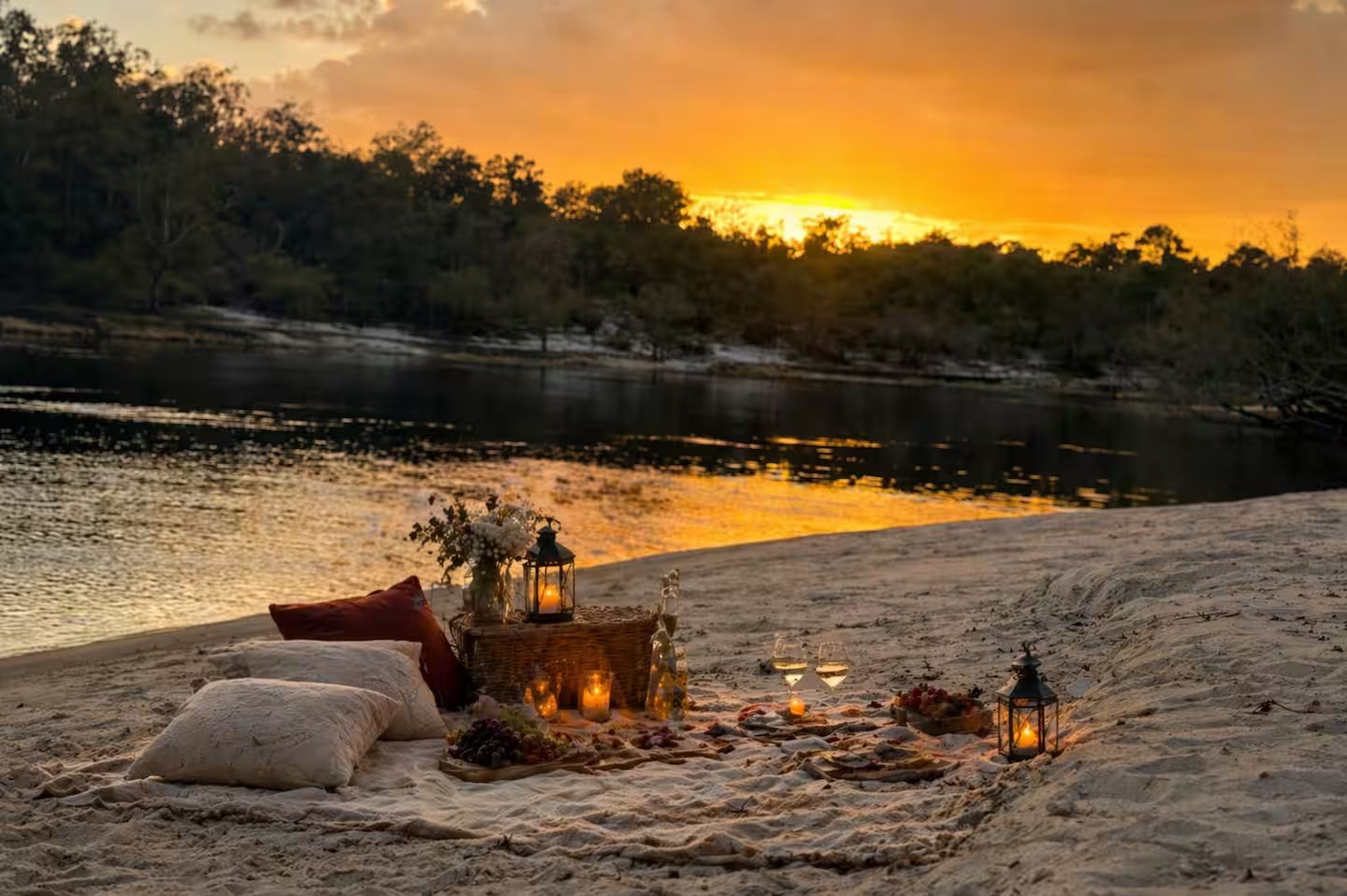 Escena de playa con un montaje para picnic que incluye una cesta de frutas, un farol y una manta.