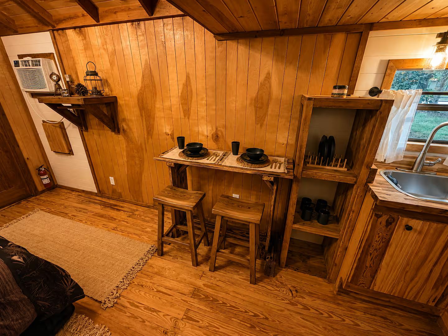 A wooden interior with a dining table set for two, a kitchen area with a sink, and a fire extinguisher on the floor.