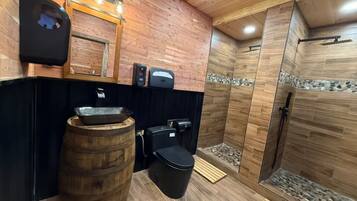 Ein Badezimmer mit einem Waschbecken aus Holzfässern, einer schwarzen Toilette und einer Duschkabine mit Holzwänden und einem Steinakzent.