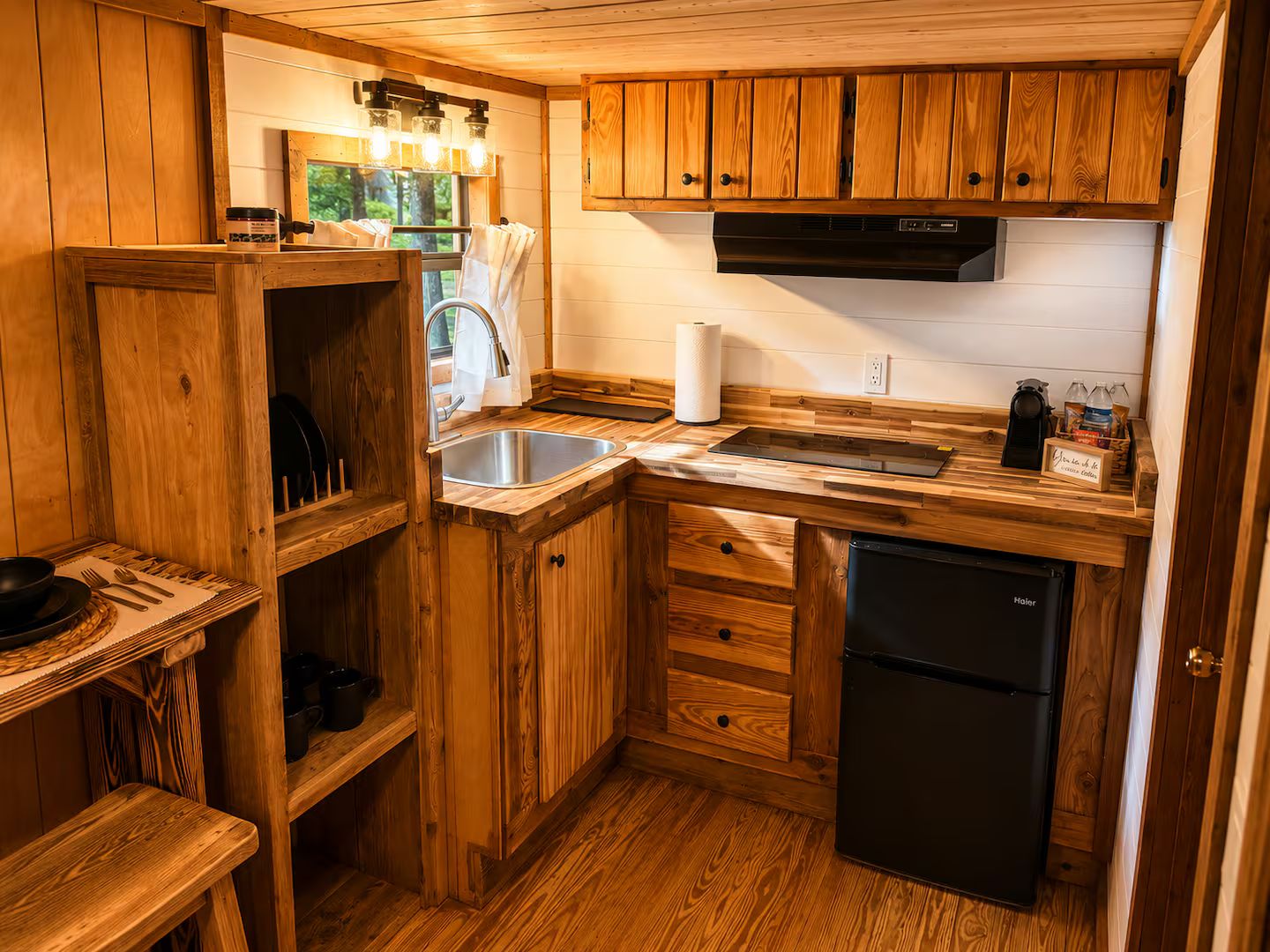Una cocina compacta con armarios de madera, un lavamanos de acero inoxidable y un refrigerador negro.