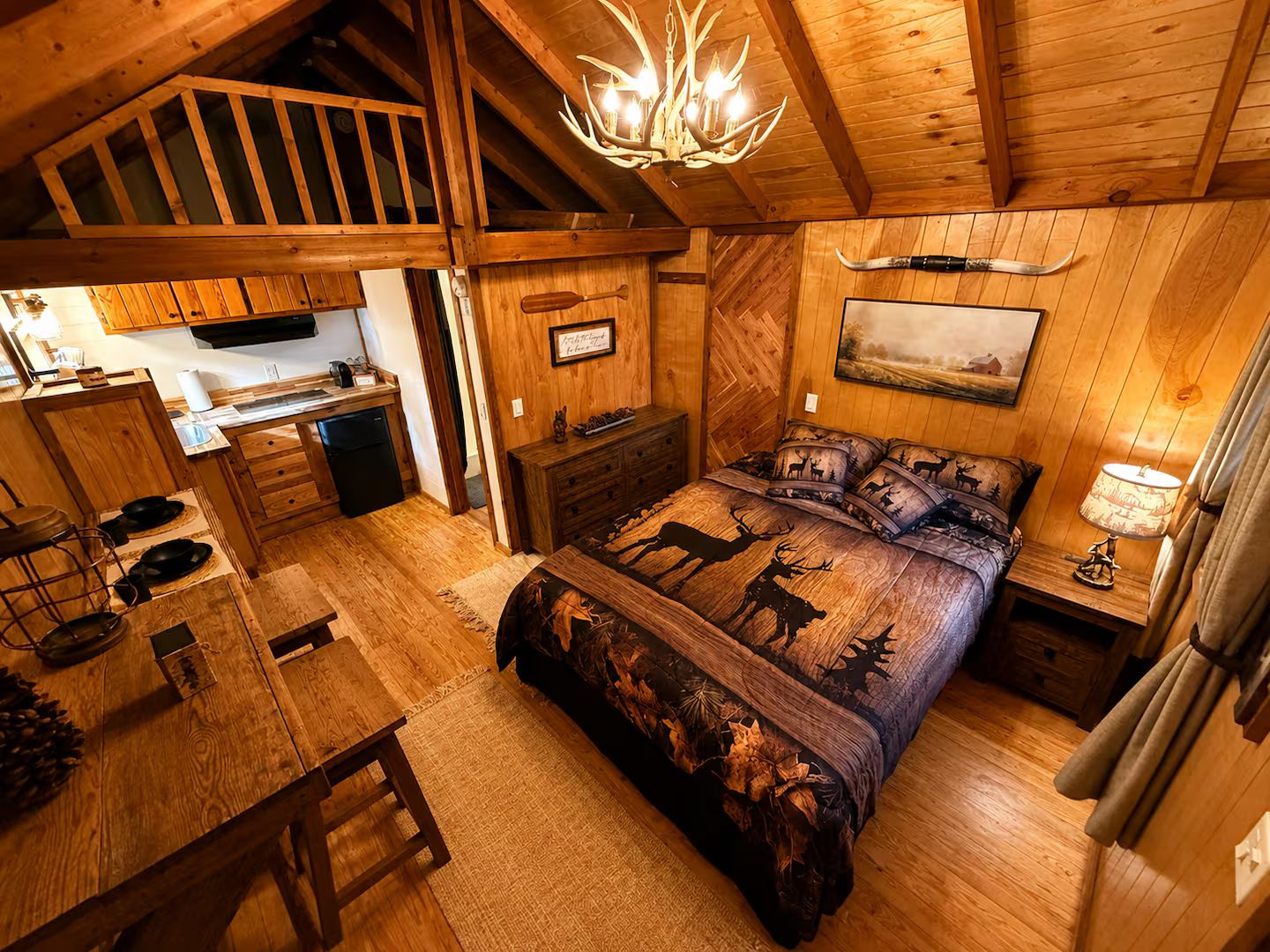 Ein Blockhaus-Interieur mit einer Erkerküche, einem Bett mit Hirschmuster und einem Kronleuchter.