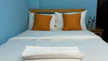 A neatly made bed with white linens and two orange pillows, a wooden headboard, and a nightstand with water bottles.