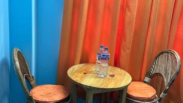 A room with two wicker chairs and a small wooden table, each with a cushion. There are two bottles of water on the table.