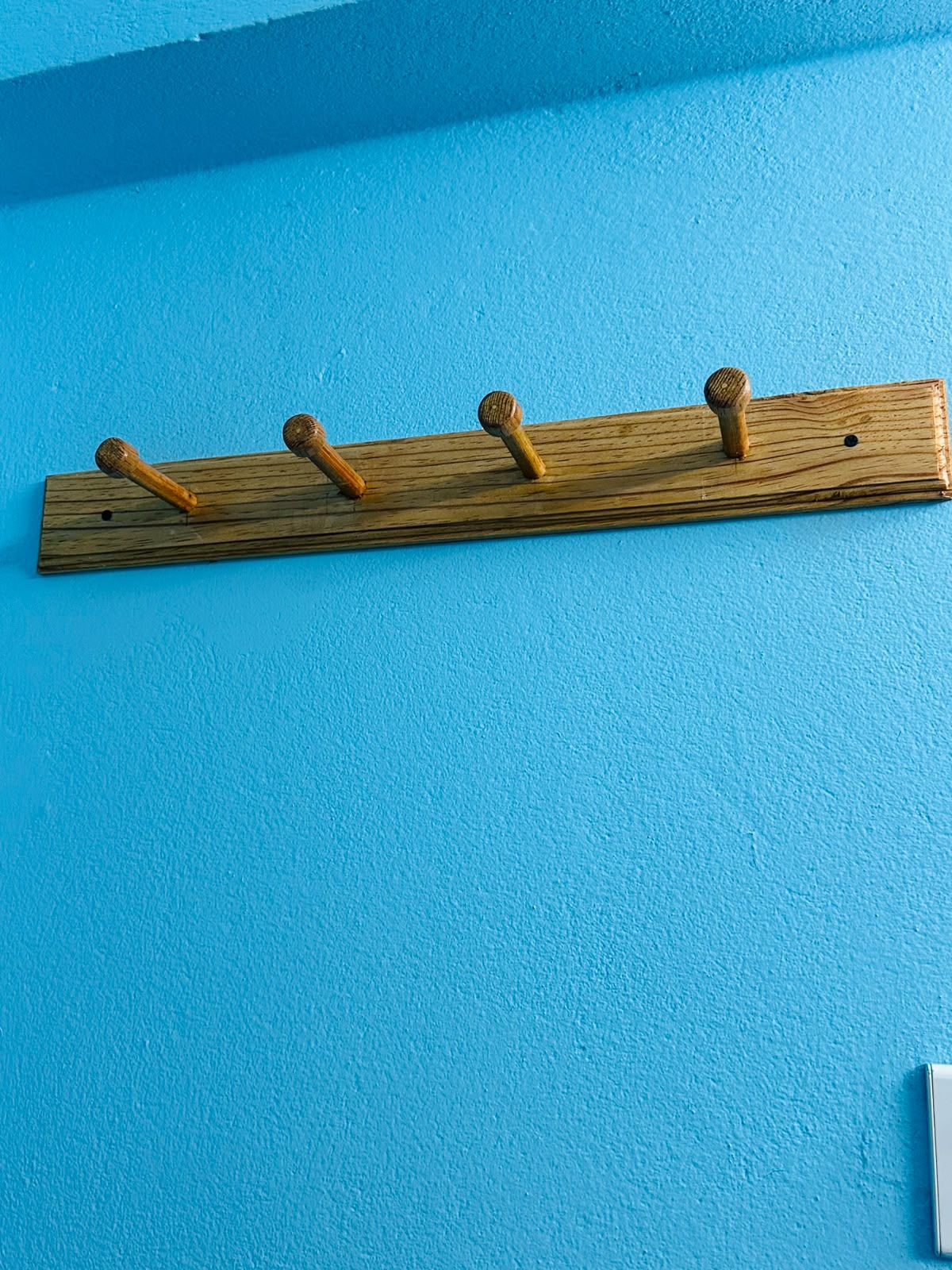 A wooden coat rack with four hooks against a blue wall.