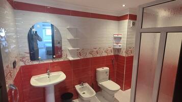 A bathroom with a white sink, a bidet, a toilet, and a shower area.