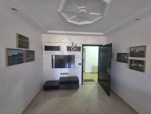 Una habitación con una televisión de pantalla plana instalada en una pared texturizada, un banco y cuadros en las paredes.