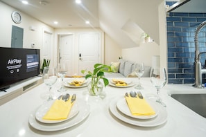 A dining area with a table set for four, a television displaying an AirPlay interface, and a blue-tiled wall.
