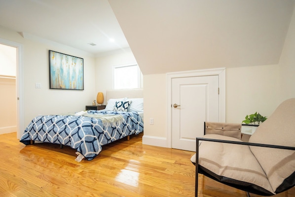 A bedroom with a bed, a chair, a door, and a painting on the wall.