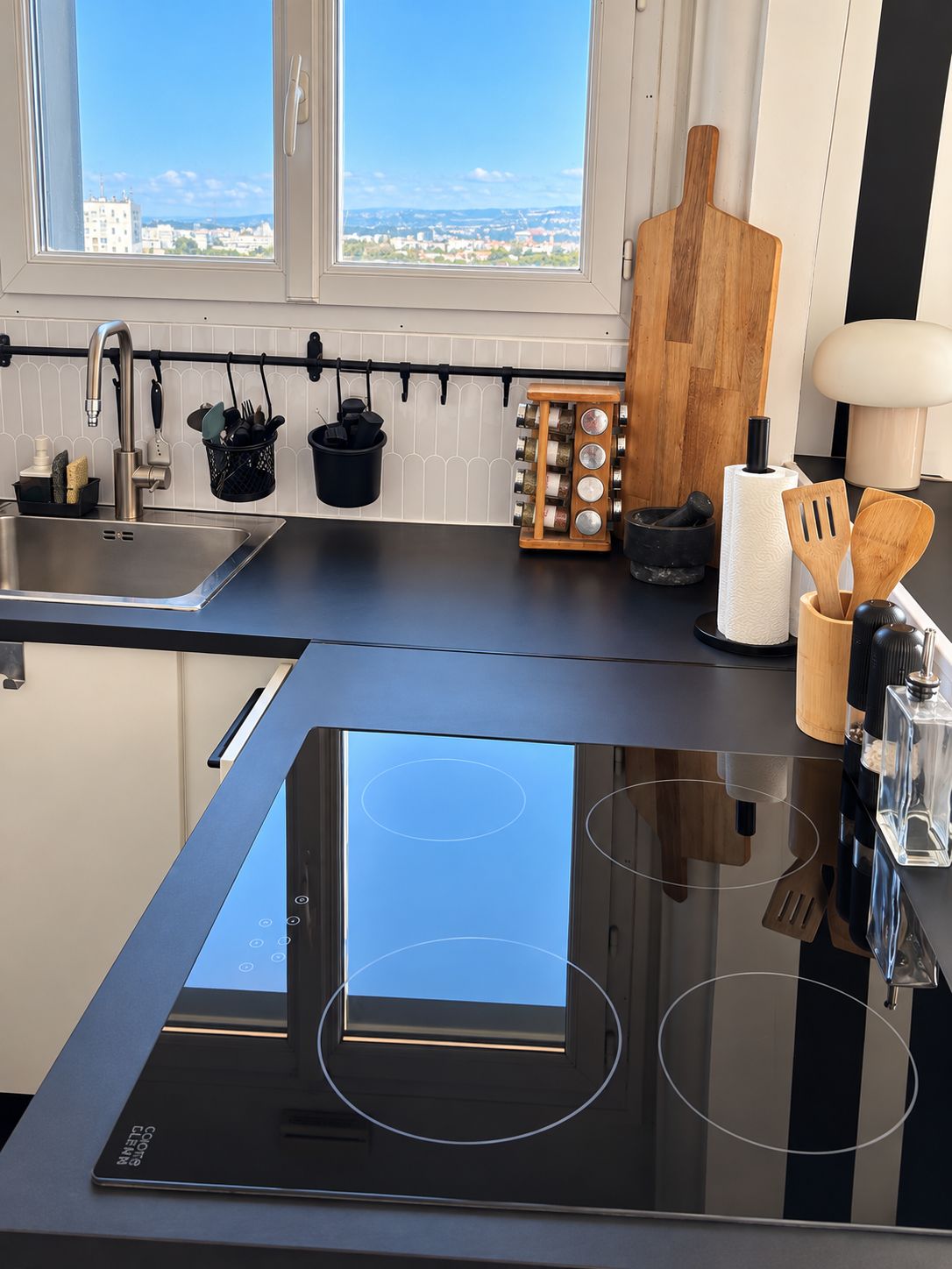 A modern kitchen with a built-in induction cooktop, a stainless steel sink, and a window with a city view.
