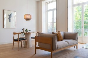 Ein modernes Wohnzimmer mit einer Couch, einem Esstisch mit Stühlen, einer Pendelleuchte und einem großen Fenster mit Blick auf Grünflächen.