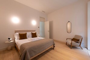 Ein modernes Schlafzimmer mit einem großen Bett, Nachttischen, einem Sessel und einem Spiegel an der Wand.