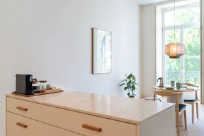 A kitchen with a coffee machine, a plant, and a dining area with chairs and a table. - Tripas-Coração: Mouzinho32 1st Floor Apt D (Porto)