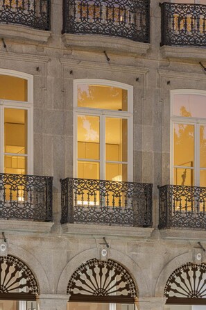 Eine Gebäudefassade mit drei großen Fenstern, jedes mit einem Balkon und aufwendig gestalteten schmiedeeisernen Geländern.