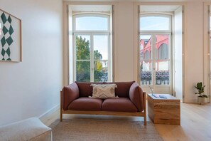 Ein Wohnzimmer mit einem braunen Sofa, einem Holztisch und einem großen Fenster mit Blick auf Gebäude.
