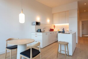 A modern kitchen with white cabinetry, a central island, and a round dining table with chairs. - Tripas-Coração: Mouzinho32 2nd Floor Apt E (Porto)