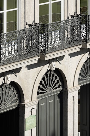 A building facade with ornate wrought iron balcony railings, arched windows, and a sign indicating the address. - Tripas-Coração: Mouzinho32 1st Floor Apt E (Porto)