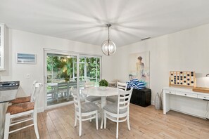 A dining area with a round table and white chairs, a ceiling light fixture, and a view through glass doors to an outdoor garden. - Upscale and Inviting Naples Home Near the Beach (Naples)