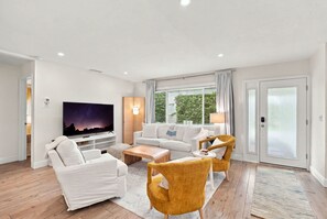 A modern living room with a flat-screen TV, white sofas, a coffee table, and a yellow armchair. - Upscale and Inviting Naples Home Near the Beach (Naples)