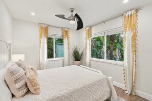A bedroom with a bed, curtains, a ceiling fan, and windows with a view of greenery. - Upscale and Inviting Naples Home Near the Beach (Naples)