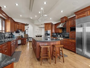 A spacious kitchen with wooden cabinets, stainless steel appliances, and a central island with bar stools. - Luxurious Private Villa: 8BR, 15 Bath & Bar (Foxfield)