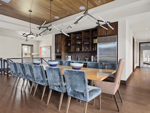 Een moderne eetruimte met een houten tafel, blauwe bekleden stoelen, en een keuken met donker houten kastjes en een roestvrijstalen koelkast.