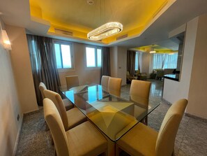 A conference room with a glass table and six chairs, a chandelier, and large windows with curtains. - VESTA  - Superior Suite - 2BR - Partial Nile View (Cairo)