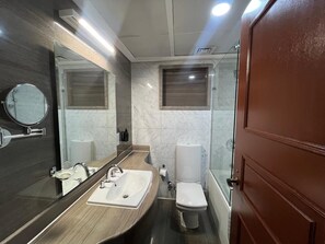 A modern bathroom with a large mirror, a sink, a toilet, and a shower area. - VESTA  - Superior Suite - 2BR - Partial Nile View (Cairo)