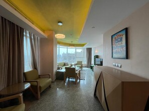 A hotel room with a seating area, a dining table, and a large window offering a city view. - VESTA  - Superior Suite - 2BR - Partial Nile View (Cairo)
