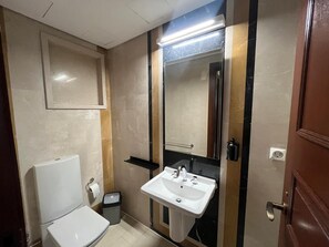 A compact bathroom with a toilet, sink, mirror, and a trash bin. - VESTA  - Superior Suite - 2BR - Partial Nile View (Cairo)