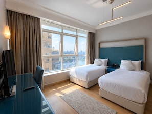 A hotel room with two beds, a desk, and a large window with curtains. - VESTA  - Superior Suite - 2BR - Partial Nile View (Cairo)